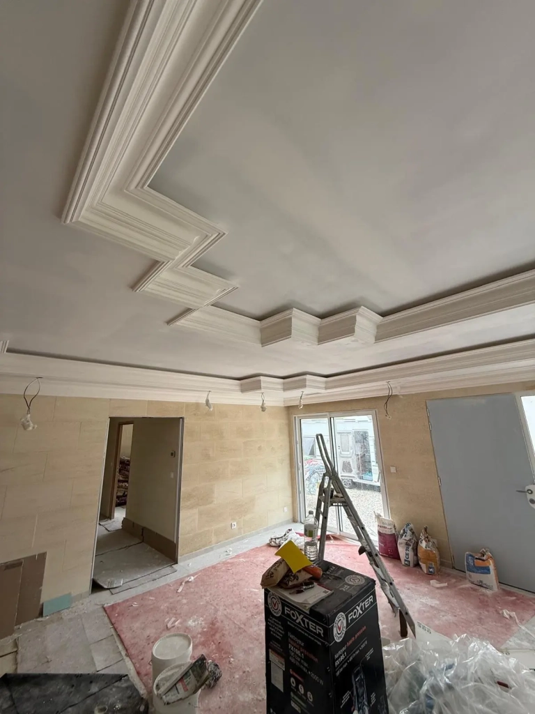 Plafond décoratif avec moulures et faux plafond en cours de rénovation dans une maison moderne.